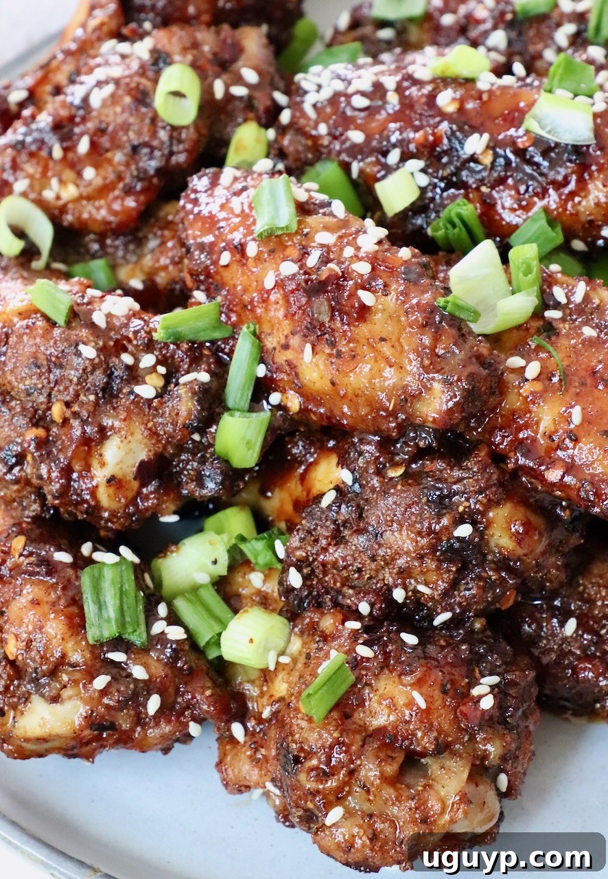 Cooked General Tso chicken wings tossed in sauce, piled high on a plate and garnished with diced green onions and sesame seeds