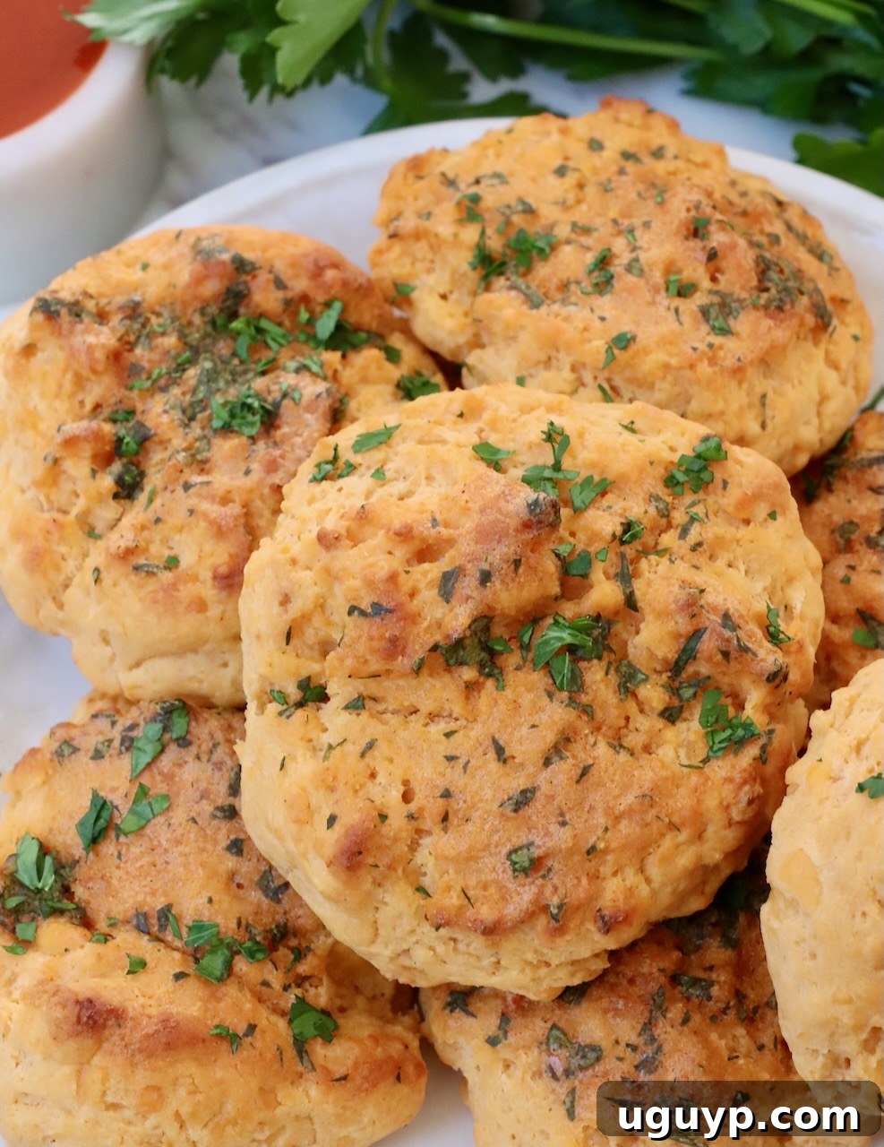 cheddar biscuits stacked up on a plate topped with fresh chopped parsley
