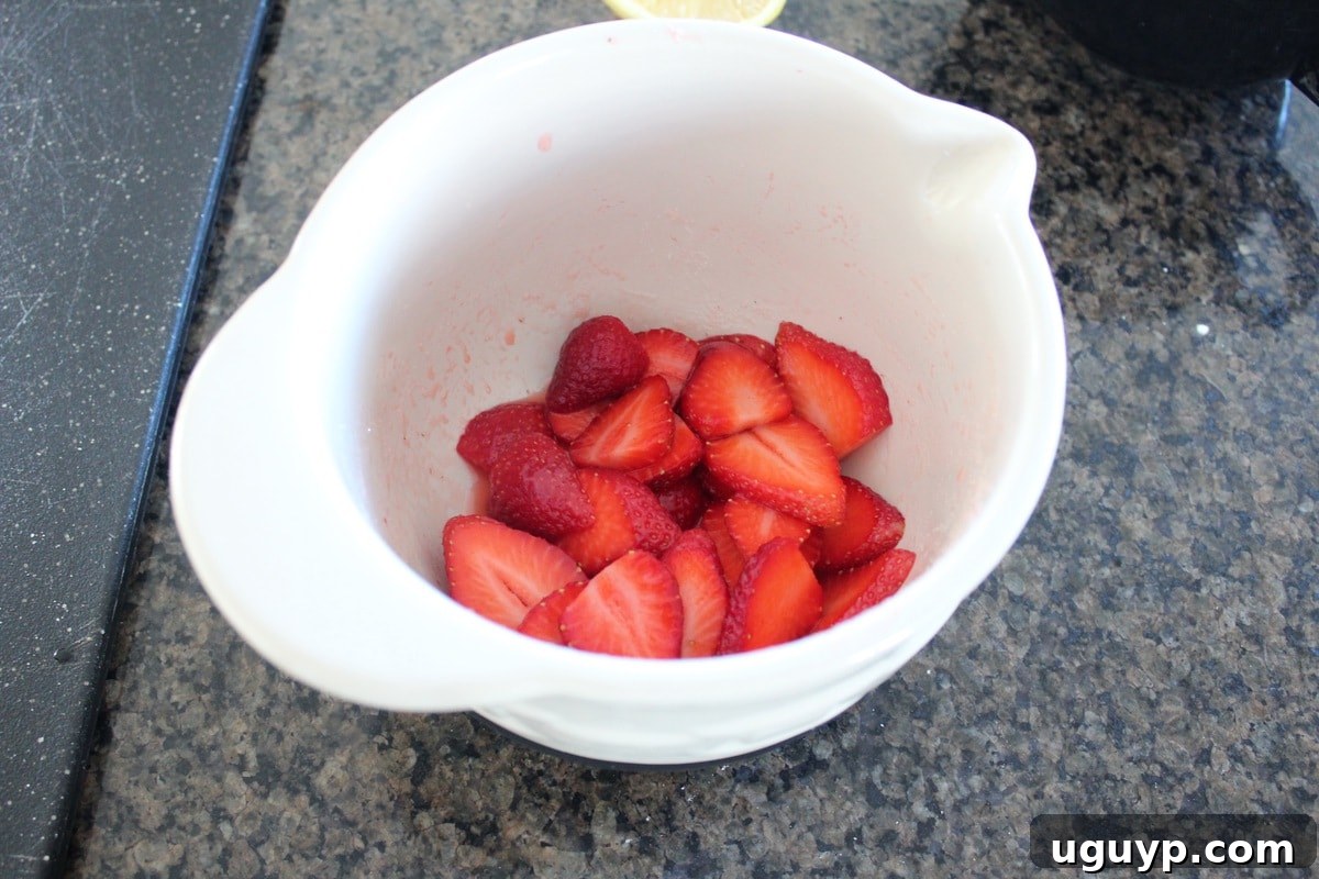 Sliced strawberries being mixed with sugar and lemon juice