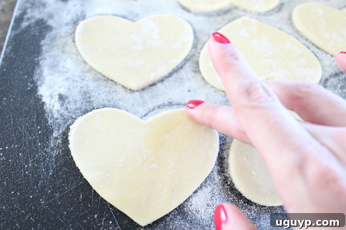 Brushing egg wash on the edges of heart-shaped puff pastry