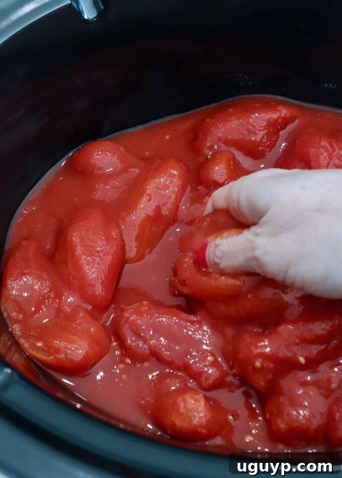 hand reaching into slow cooker filled with whole canned tomatoes