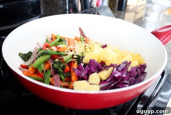 Adding garlic, ginger, red cabbage, and pineapple to sautéed vegetables