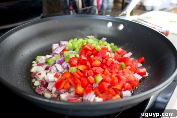 Chopped onions, red bell peppers, and green bell peppers sautéing in a skillet.