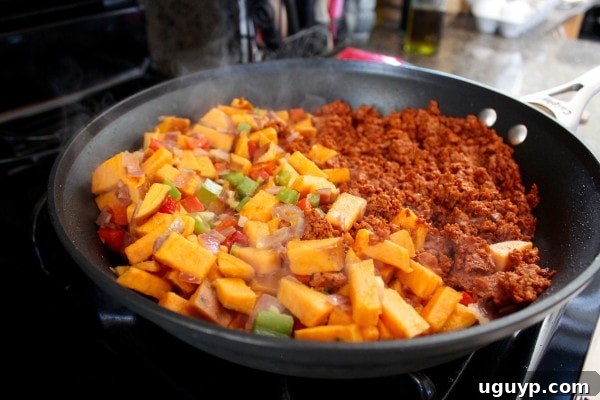 Soyrizo, bell peppers, and sweet potatoes cooking together in a large skillet.