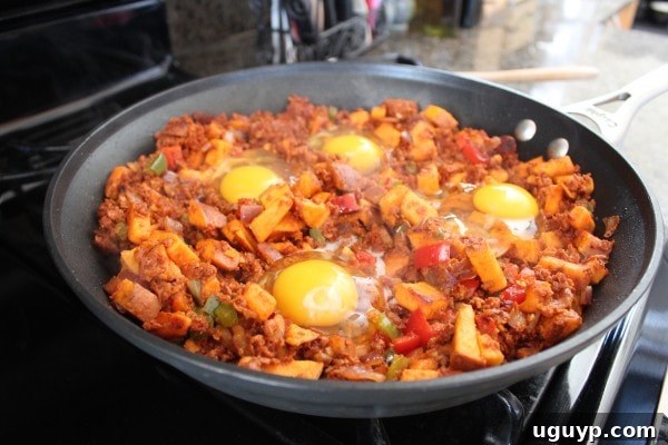 Four eggs cracked directly onto the Mexican Sweet Potato Hash in a skillet, ready to be covered and cooked.