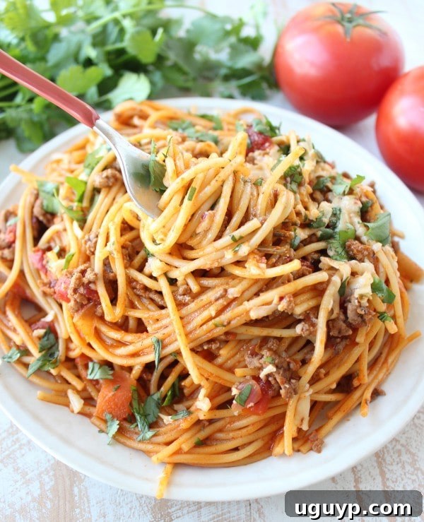 A fork scooping up a bite of One Pot Buffalo Taco Spaghetti on a white plate, highlighting the creamy, cheesy texture.