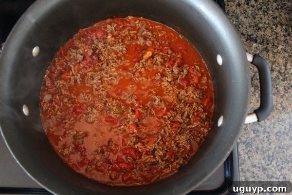 A pan filled with browned ground beef, taco seasoning, diced tomatoes with green chilies, and buffalo sauce, simmering together.