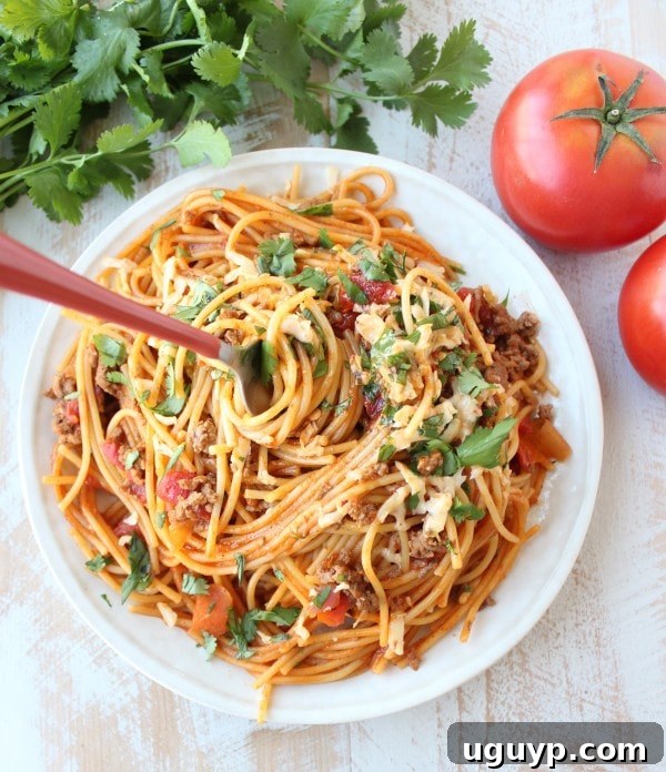A fork twirling buffalo taco spaghetti on a white plate, showcasing the sauce-coated noodles and melted cheese.
