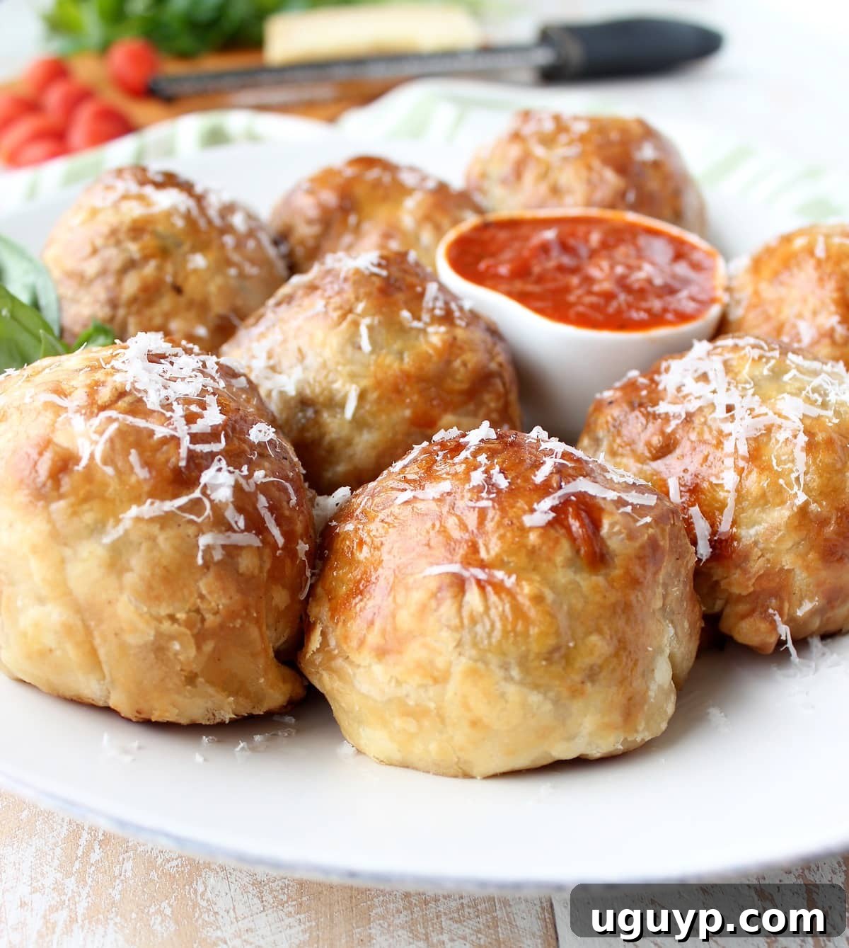 Puff pastry wrapped meatballs on plate topped with shredded parmesan cheese