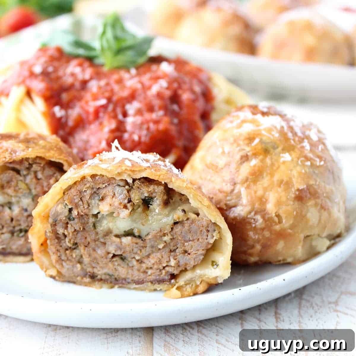 Baked puff pastry wrapped meatball cut in half on plate with spaghetti and red sauce