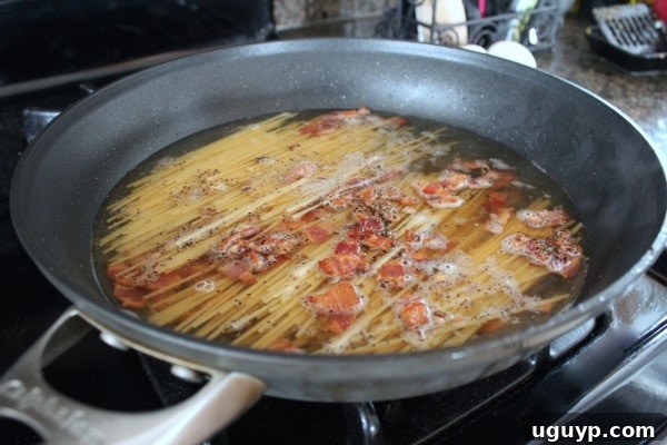 Adding spaghetti and broth to the skillet for One Pot Pasta Carbonara