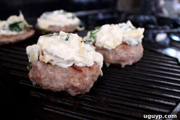 Spinach Artichoke Turkey Burgers grilling on a griddle, topped with extra dip