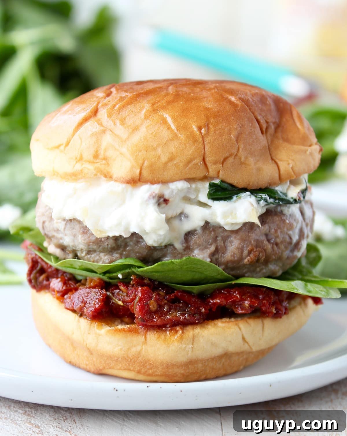 A perfectly built Spinach Artichoke Turkey Burger with sun-dried tomatoes and fresh spinach