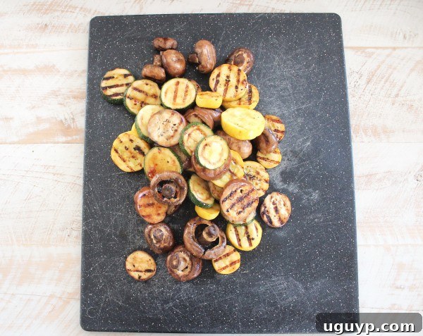 Hands chopping grilled zucchini and yellow squash on a wooden cutting board