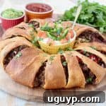 A golden Crescent Roll Taco Ring presented on a wooden cutting board, surrounded by small ramekins of sour cream, vibrant salsa, and creamy guacamole, ready for serving.