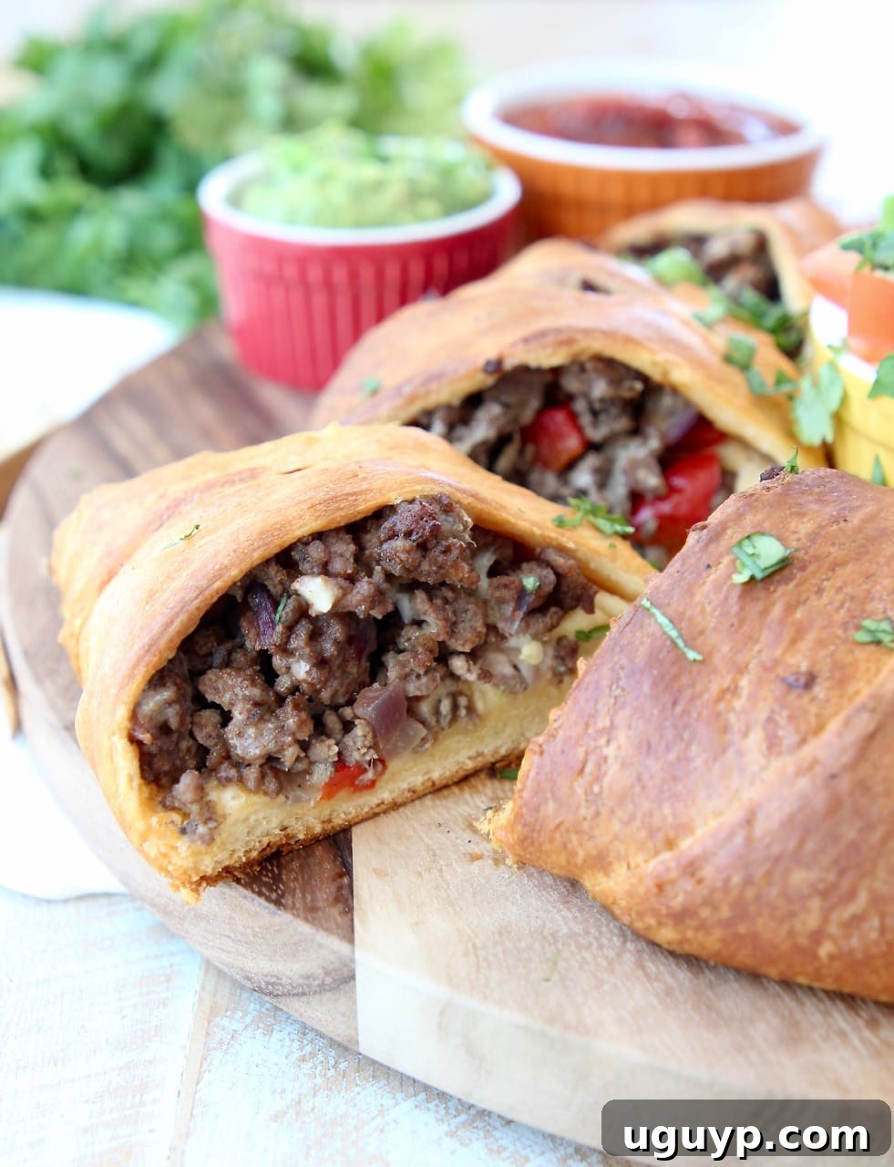 A close-up shot of a baked crescent roll taco ring on a wooden cutting board, with one slice removed, revealing the delicious ground beef, onion, and bell pepper filling. The crust is golden and flaky.