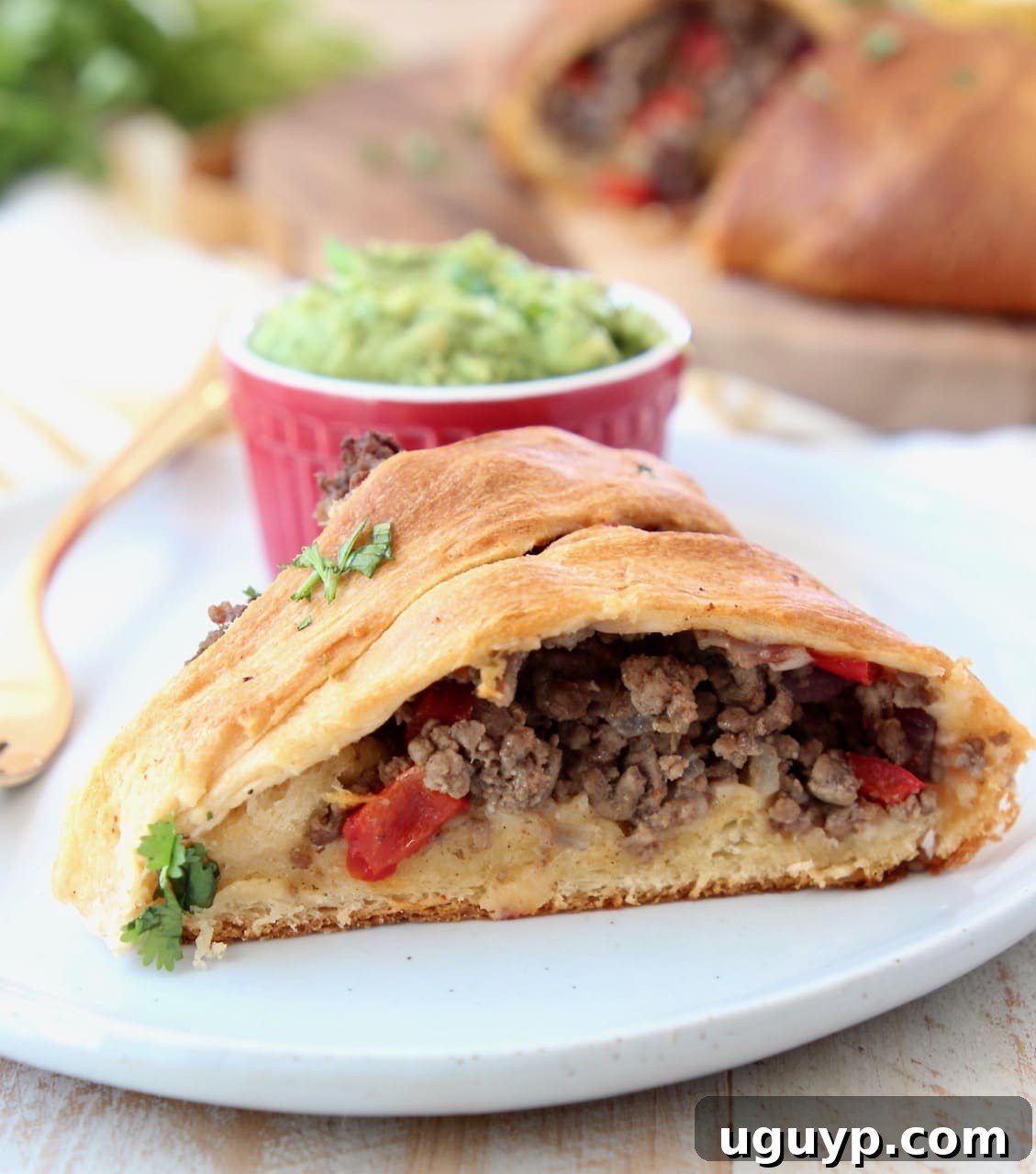 A perfectly portioned slice of crescent roll taco ring, showcasing its savory ground beef filling, served alongside a small ramekin of fresh guacamole and a gold fork, ready to be enjoyed.