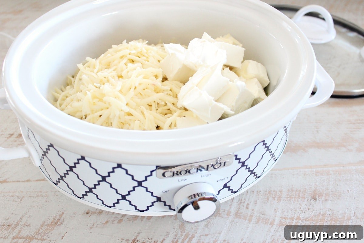 Cubed cream cheese and shredded pepper jack cheese being added to a crock pot for queso