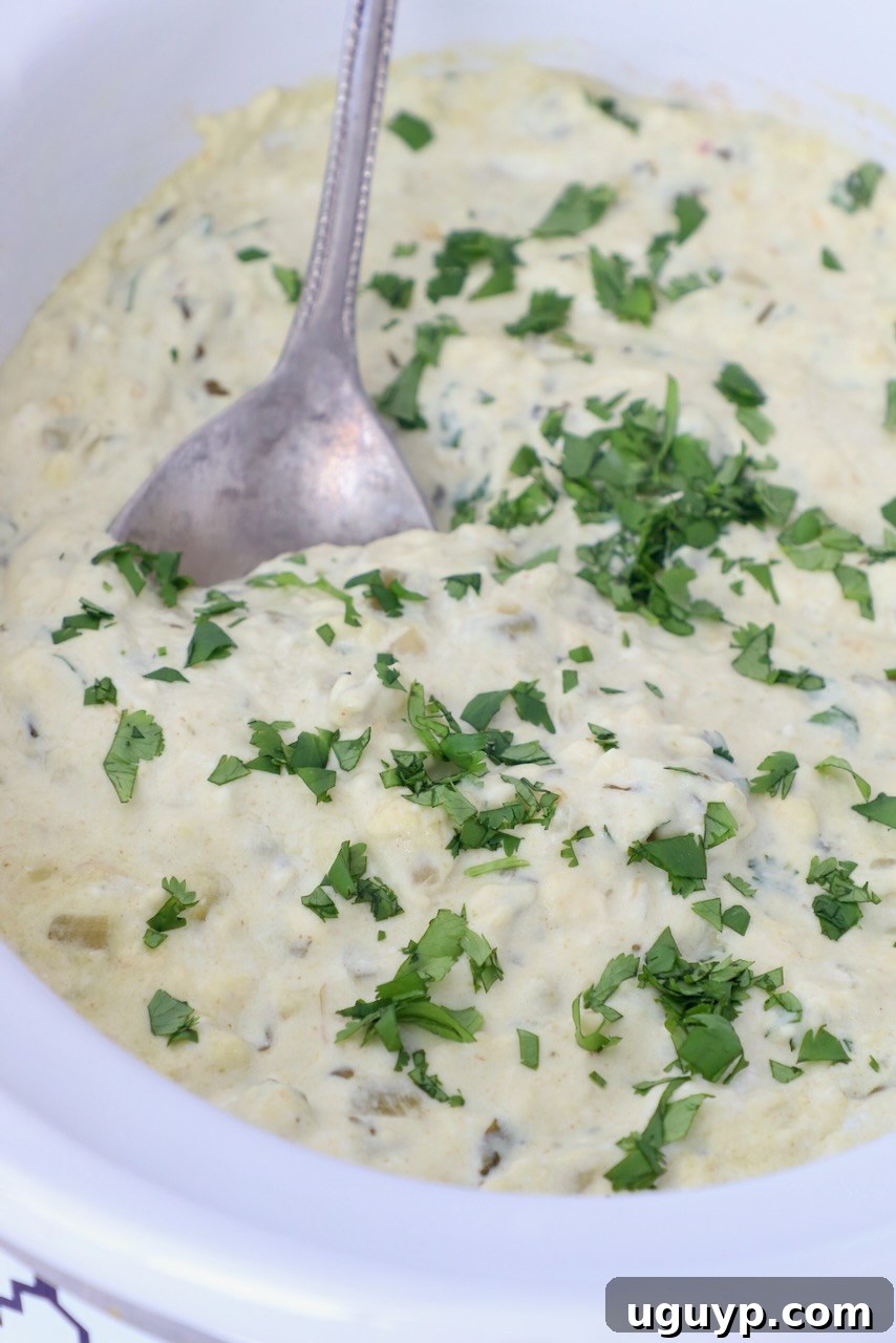 White queso dip in a slow cooker with a serving spoon, garnished with fresh cilantro