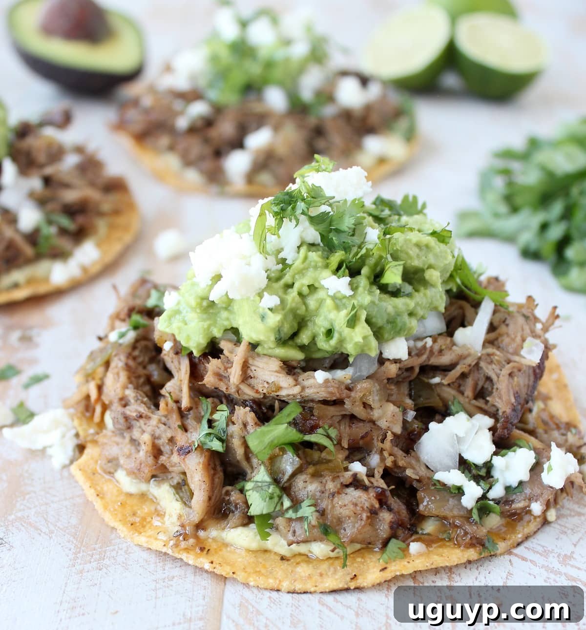 Crispy slow cooker carnitas on a tostada, topped with vibrant guacamole and cotija cheese