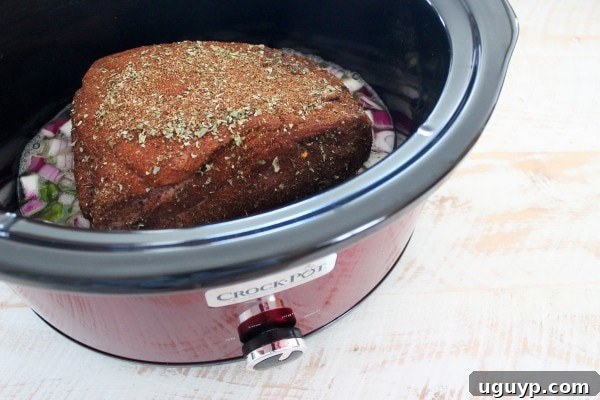 Spice-rubbed pork shoulder nestled in a slow cooker with diced onions and peppers, ready for cooking