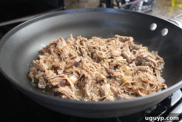 Shredded pork achieving a crispy texture in a large skillet with hot oil on the stove