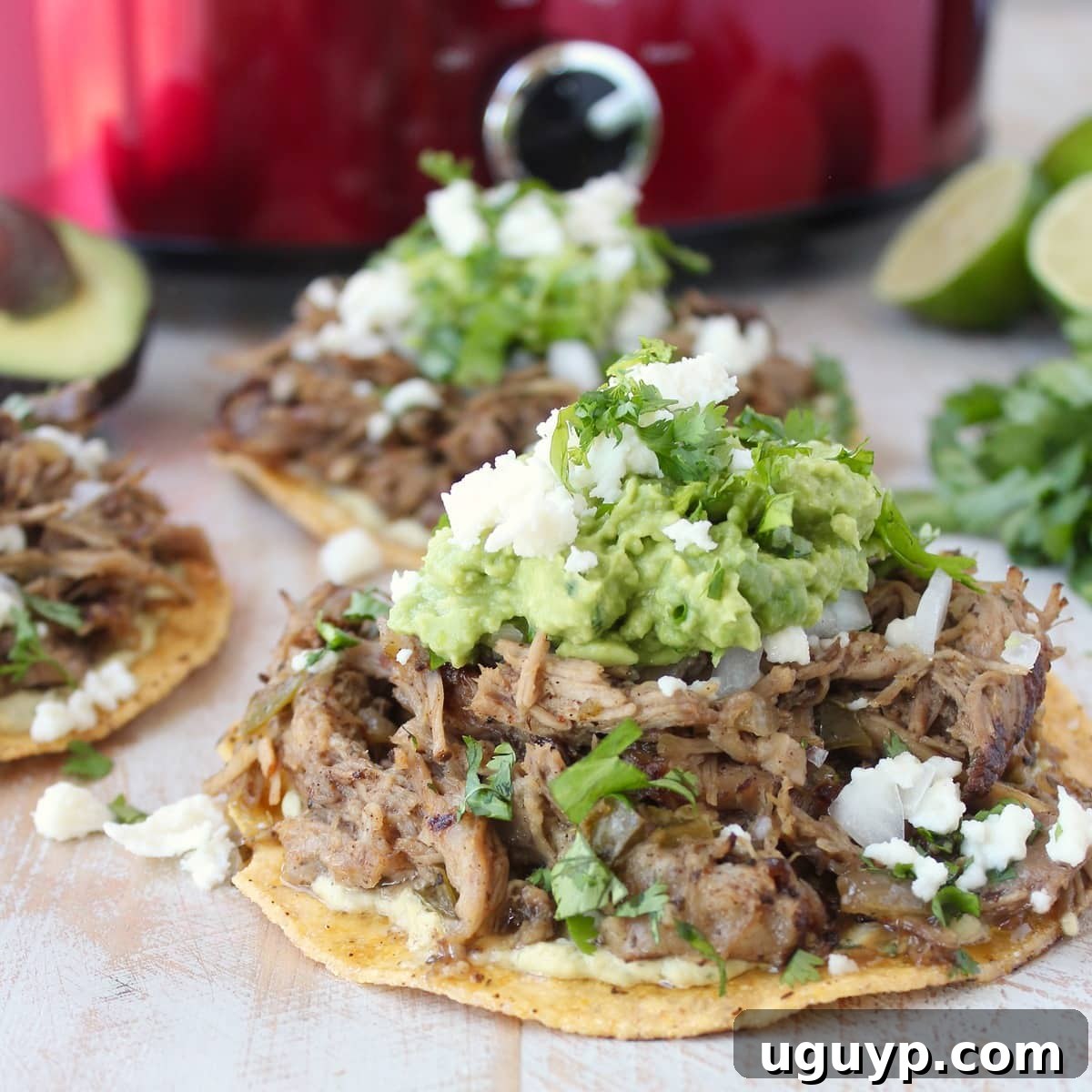 Close-up of perfectly cooked, crispy carnitas atop a tostada, garnished with creamy guacamole and crumbled cheese, ready to be enjoyed.