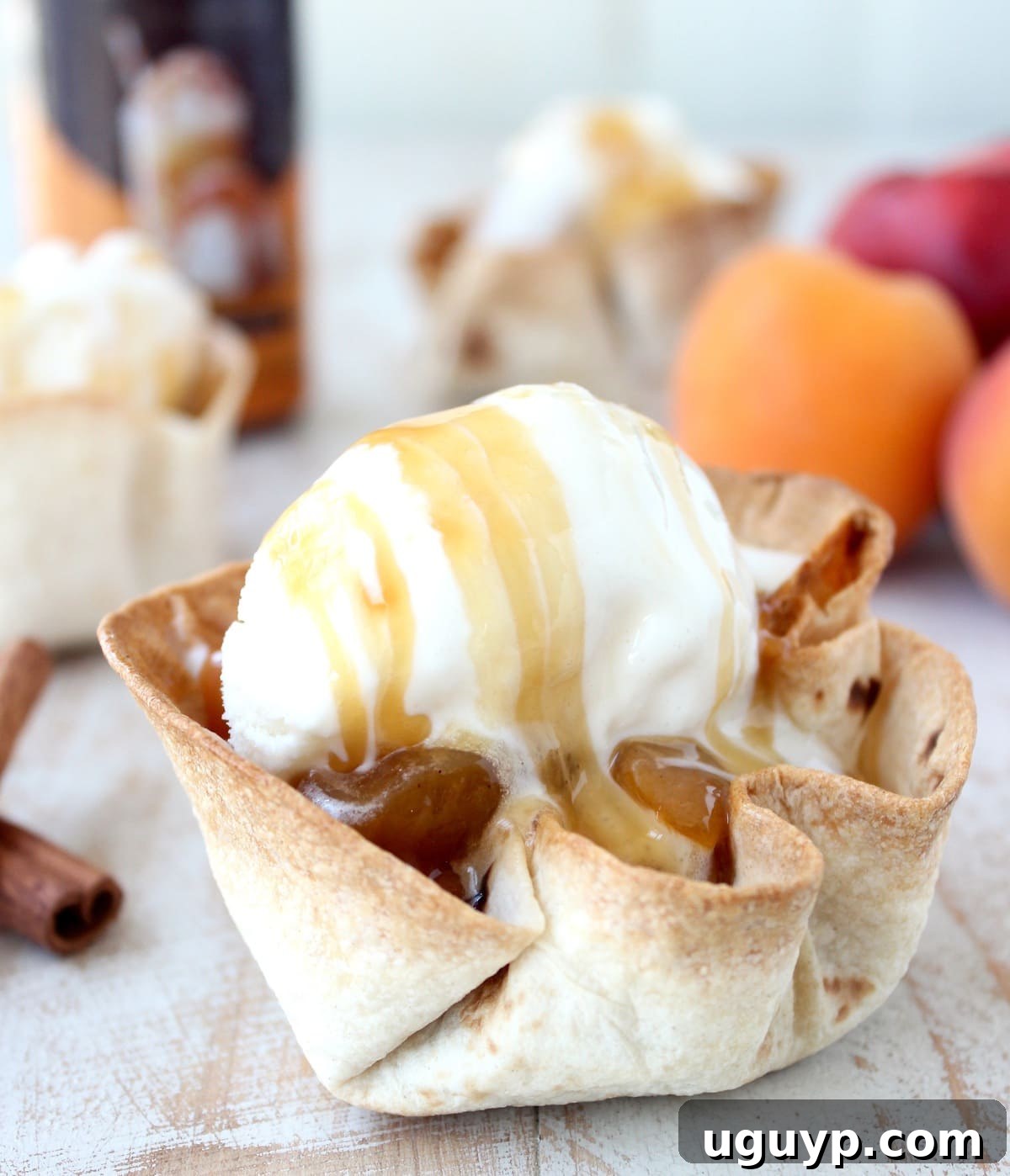 crispy taco shell cups filled with cooked fruit, topped with a scoop of ice cream and caramel syrup on a white wood board