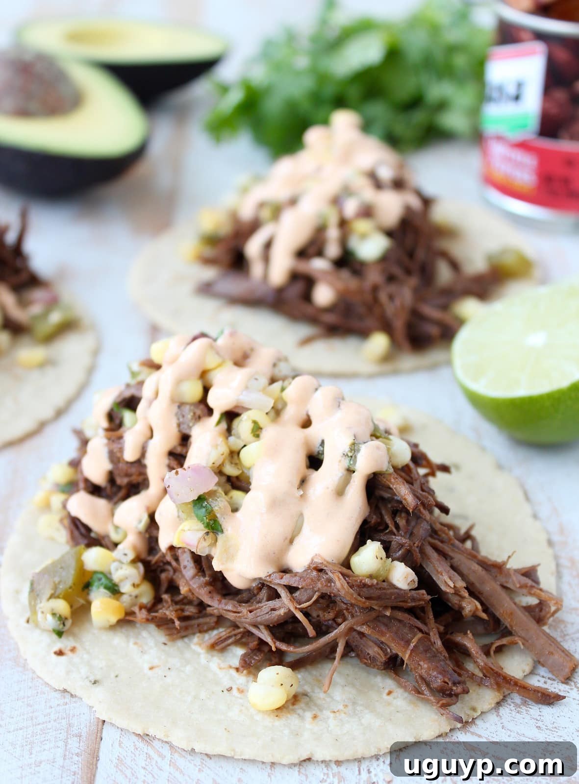 Shredded brisket tacos topped with fresh corn salsa and a drizzle of creamy chipotle sauce, arranged artfully on a serving board.