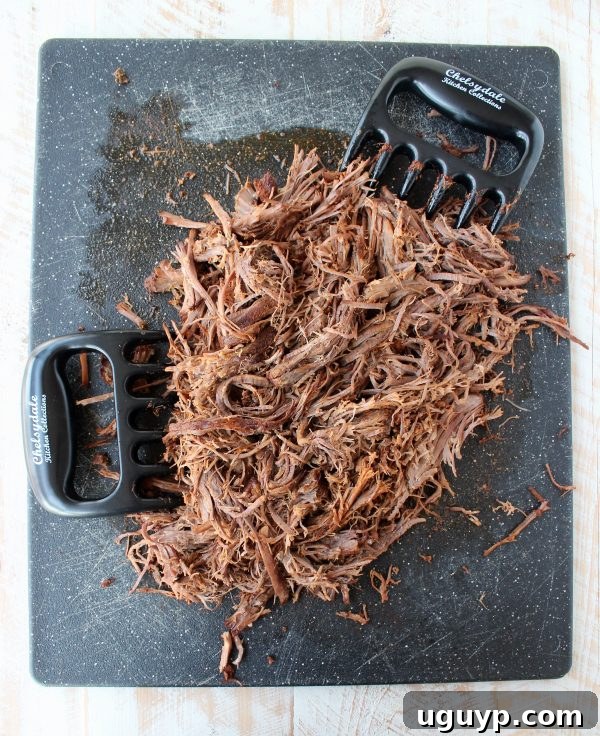 Perfectly shredded brisket on a cutting board, with meat claws visible, ready to be served in tacos.