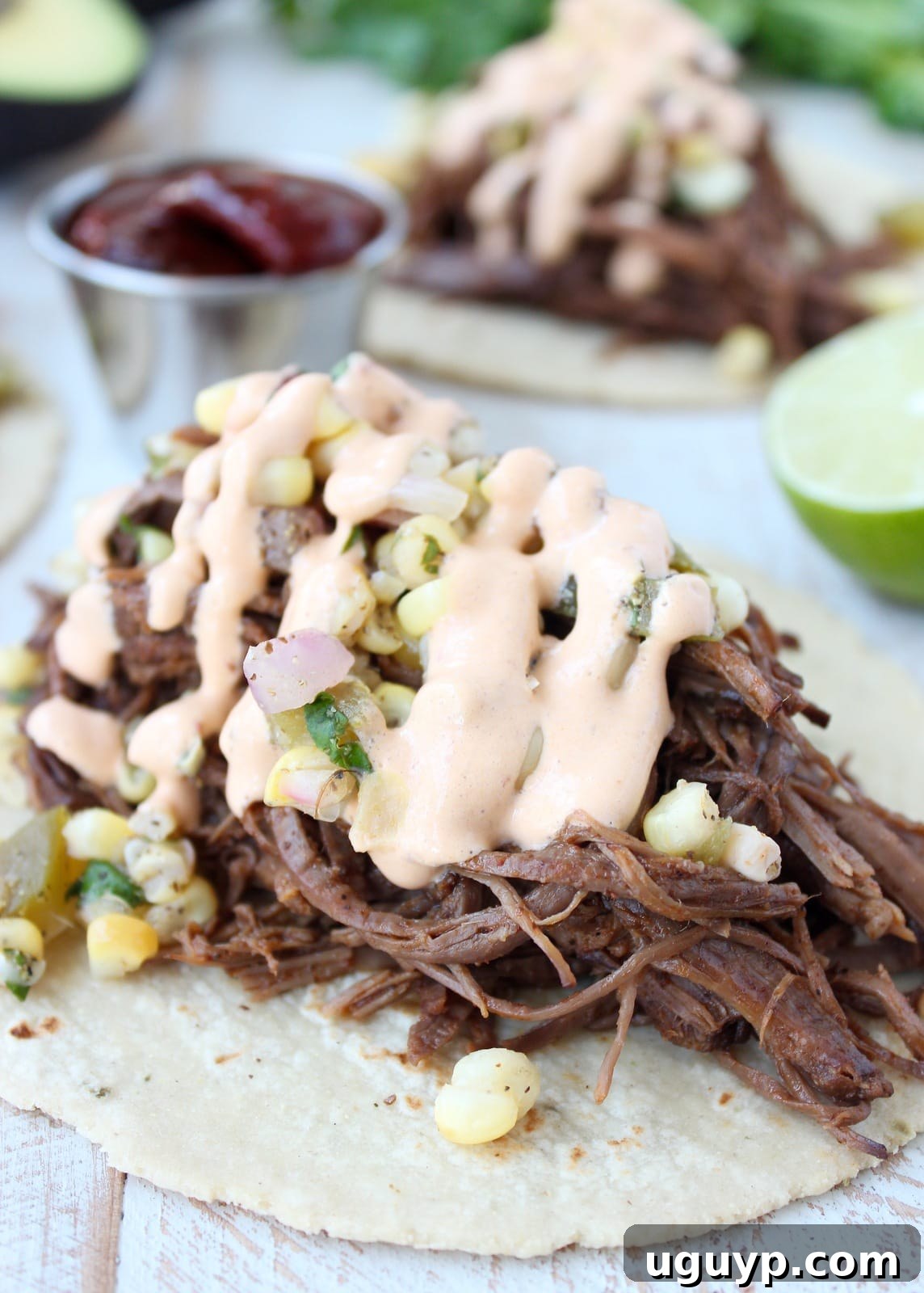A single brisket taco filled with shredded meat, topped generously with corn salsa and creamy chipotle sauce, ready to eat.