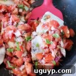cooked chicken topped with tomato bruschetta in a skillet with a red spatula
