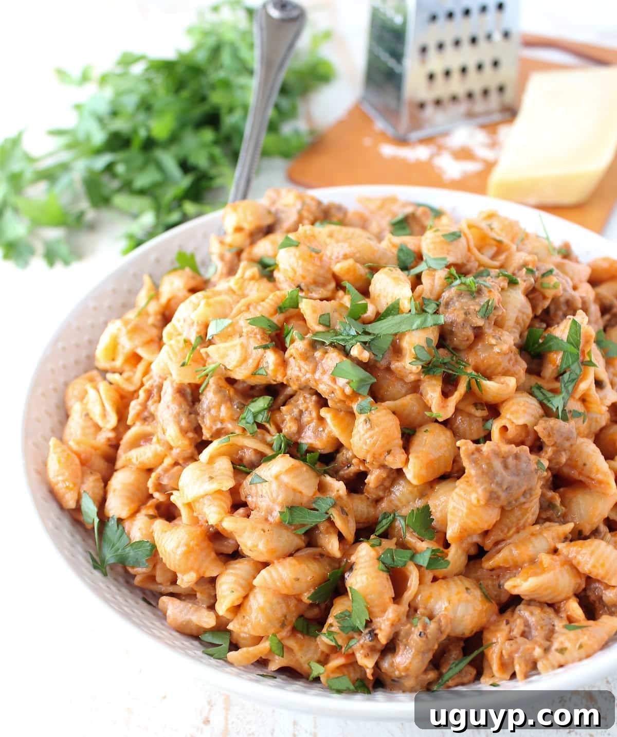 Cooked pasta shells in a cheesy sauce with sausage in a bowl with a serving spoon topped with fresh chopped parsley
