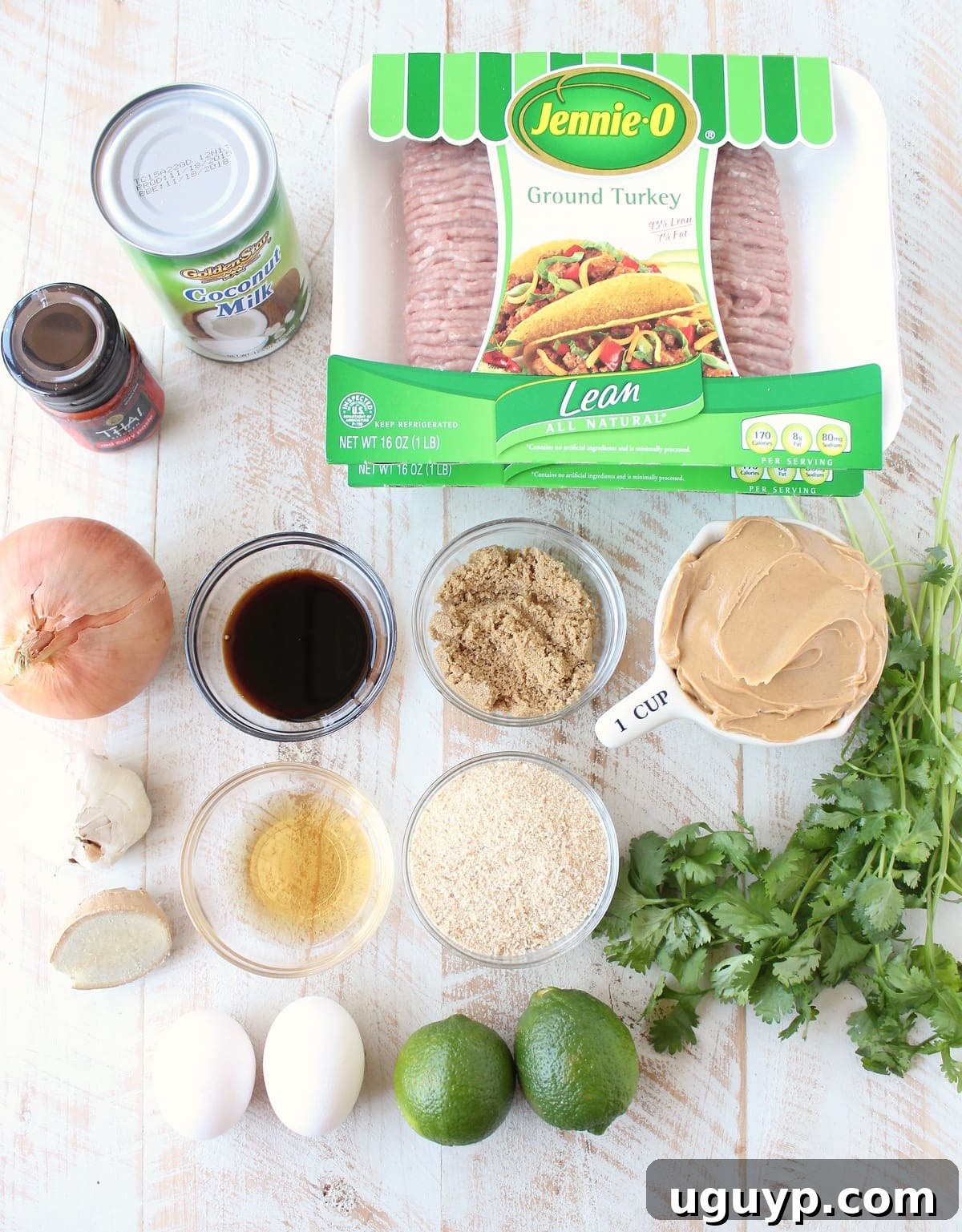 An array of fresh ingredients for Thai turkey meatballs laid out on a rustic white wooden board, including ground turkey, herbs, and spices.