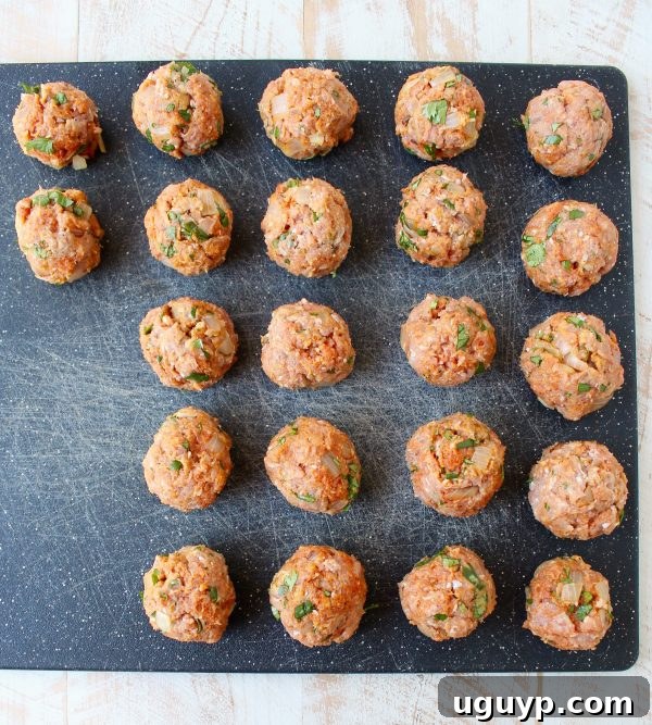 Perfectly formed uncooked turkey meatballs neatly arranged on a wooden cutting board, ready for cooking.