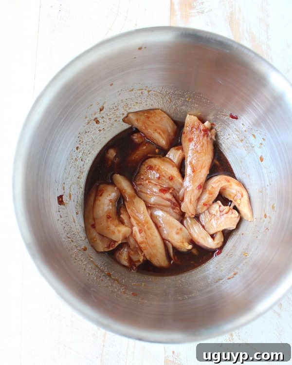 raw chicken strips tossed in sauce in a mixing bowl