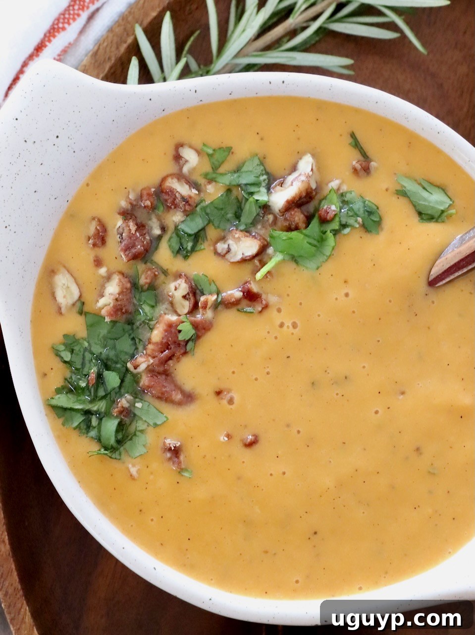 A beautifully presented bowl of sweet potato soup, garnished generously with chopped pecans and fresh parsley, sitting on a wooden surface.