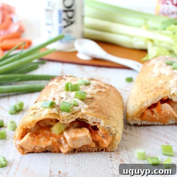Golden-brown pizza dough stuffed with cubed buffalo chicken, sliced in half to reveal the vibrant filling, resting on a rustic wooden surface.