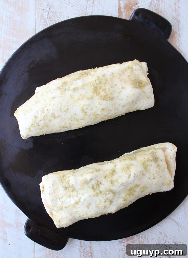 Two uncooked buffalo chicken bakes resting on a black baking stone, brushed with a seasoned butter glaze, ready to be placed into the oven.