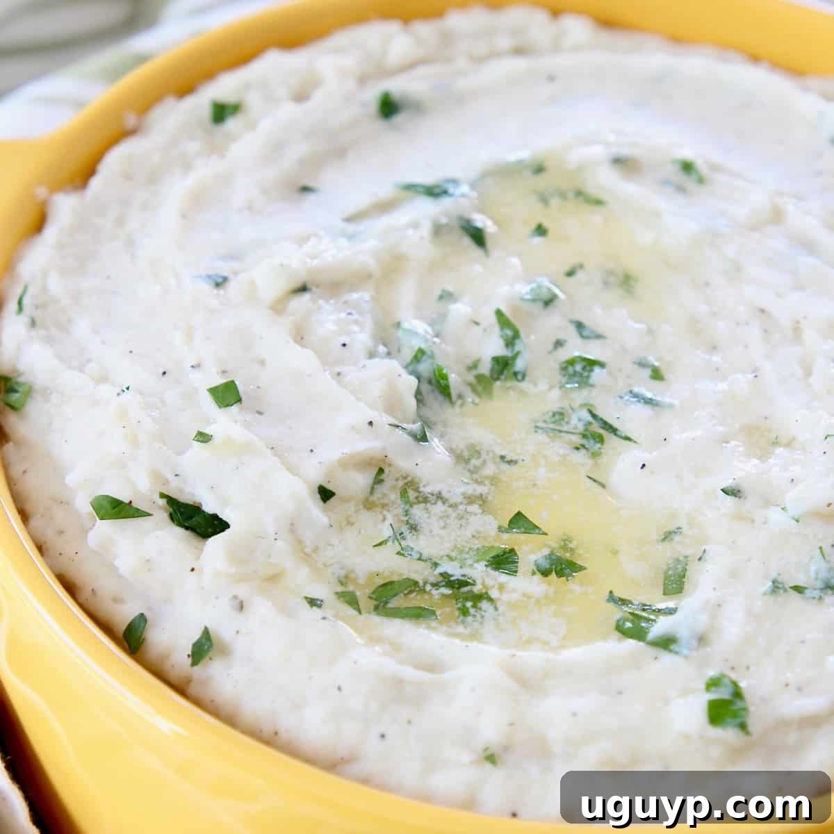 mashed potatoes topped with melted butter and chopped parsley in yellow bowl