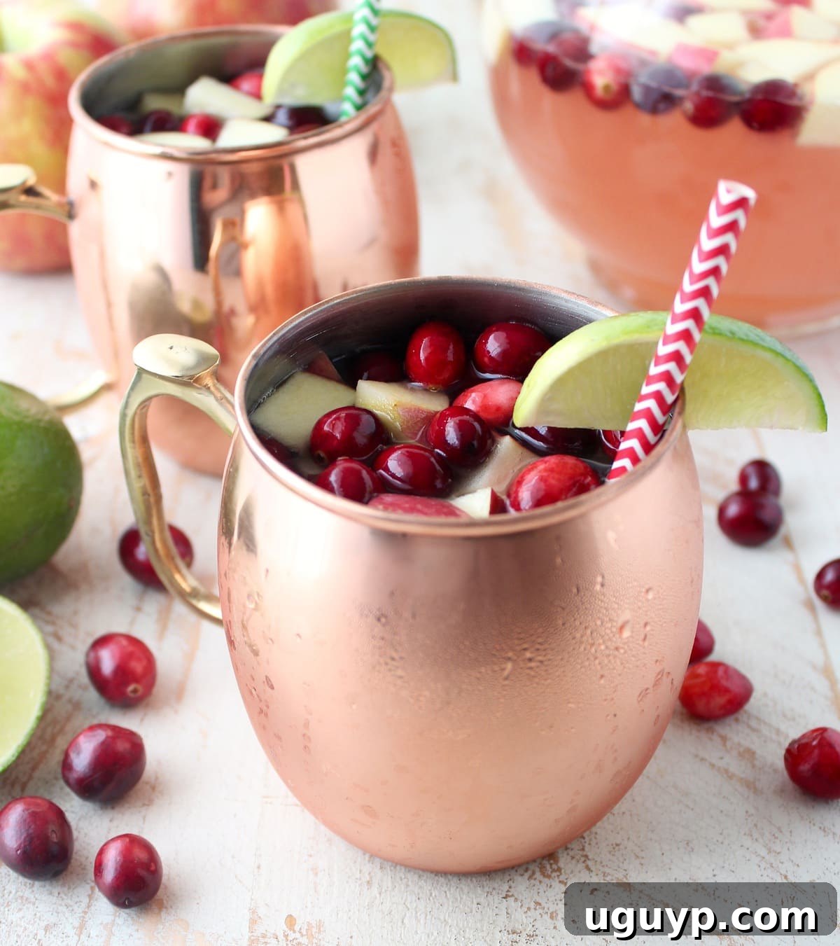 Copper mugs filled with sparkling cranberry apple Moscow Mule punch, garnished with fresh cranberries and diced apples, ready for a festive celebration.