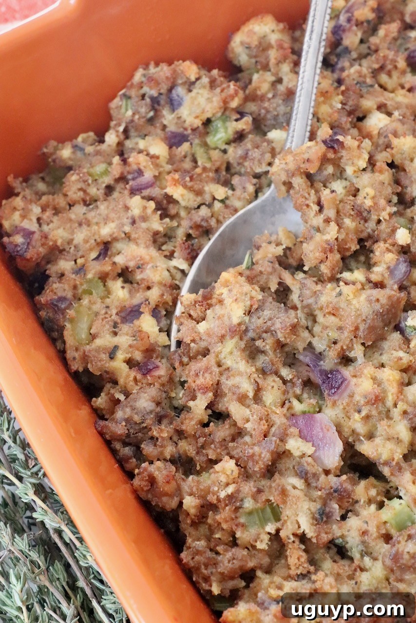 Golden brown sausage stuffing in an orange baking dish, ready to be served with a silver spoon