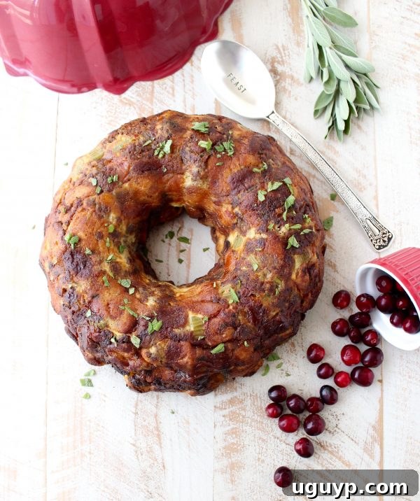 Beautifully baked sausage stuffing, shaped like a wreath from a bundt pan, garnished with fresh cranberries and rosemary on a white wooden board