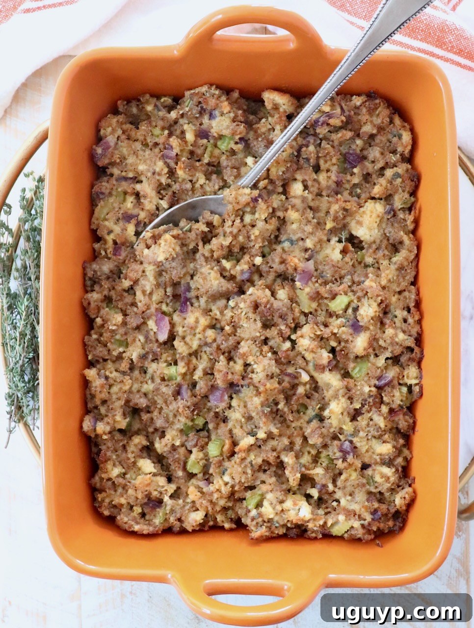 Cooked sausage stuffing, golden brown and garnished, presented in an orange casserole dish with a serving spoon