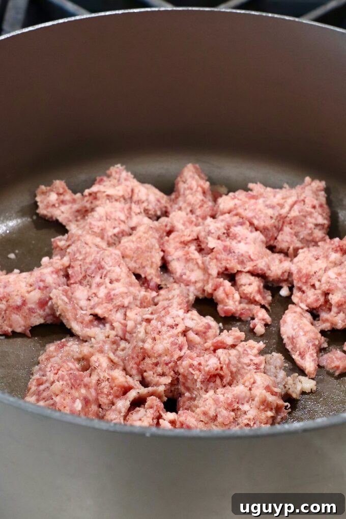 Crumbled pork sausage browning in a large pan on the stovetop
