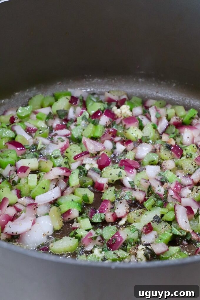 Diced red onion and celery simmering with seasonings in a large pan
