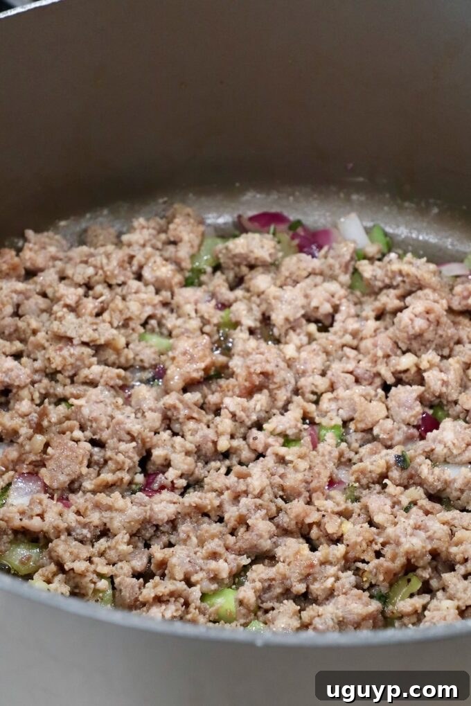 Cooked, crumbled pork sausage mixed with sautéed diced vegetables in a large pan
