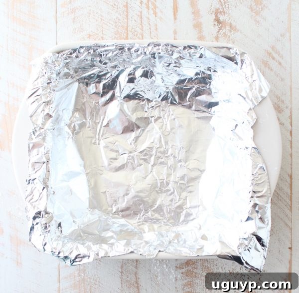 Aluminum foil carefully pressed into the puff pastry crust in a square baking dish, ready for blind baking.