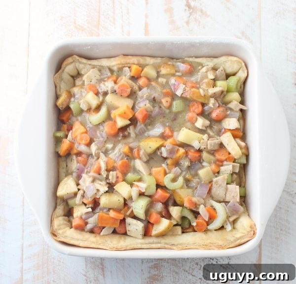 The rich, savory turkey pot pie filling, generously spooned over the pre-baked puff pastry crust in a square casserole dish, vibrant with vegetables and turkey.