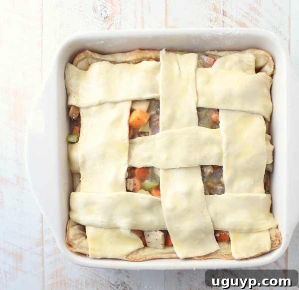 A beautifully woven lattice of puff pastry strips gracefully topping the turkey pot pie filling in a square baking dish, ready for its final bake.